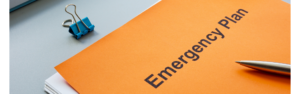 Photo of a stack of papers with a bright orange cover that reads, "Emergency Plan." A binder clip and pen tip are also present.